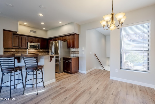 kitchen with appliances with stainless steel finishes, backsplash, dark stone counters, pendant lighting, and a breakfast bar area