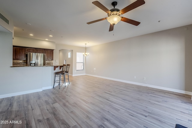 unfurnished living room with ceiling fan with notable chandelier and light hardwood / wood-style flooring