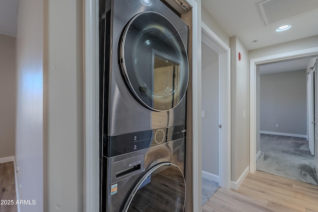 laundry room featuring stacked washer and dryer and light hardwood / wood-style flooring