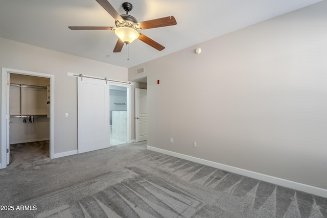 unfurnished bedroom with carpet, ceiling fan, a barn door, a spacious closet, and a closet