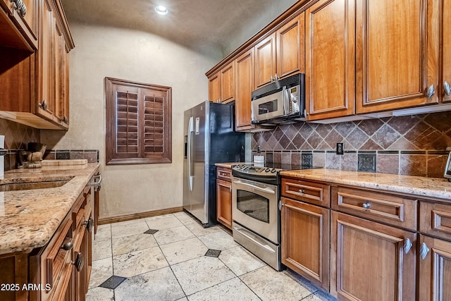 kitchen with backsplash, light stone countertops, sink, and stainless steel appliances