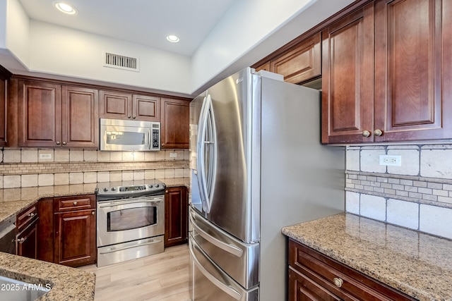 kitchen with tasteful backsplash, light stone countertops, light hardwood / wood-style flooring, and appliances with stainless steel finishes