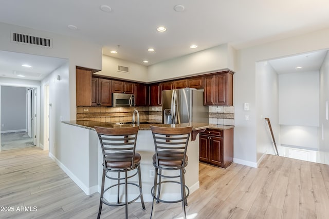 kitchen with a breakfast bar, light hardwood / wood-style floors, stainless steel appliances, and tasteful backsplash