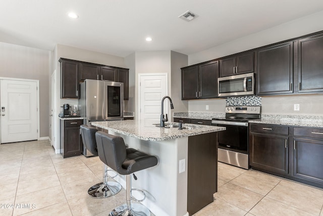 kitchen featuring sink, light tile patterned floors, an island with sink, dark brown cabinets, and stainless steel appliances