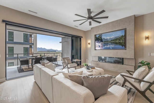 living room featuring visible vents, ceiling fan, a fireplace, and light wood finished floors