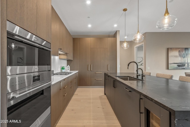 kitchen with light wood finished floors, a spacious island, appliances with stainless steel finishes, modern cabinets, and a sink