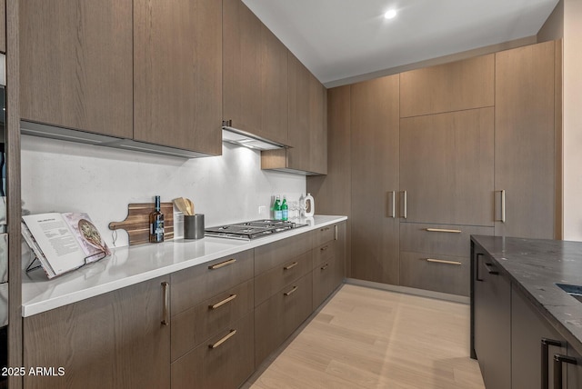 kitchen featuring light stone counters, stainless steel gas stovetop, light wood-style floors, under cabinet range hood, and modern cabinets