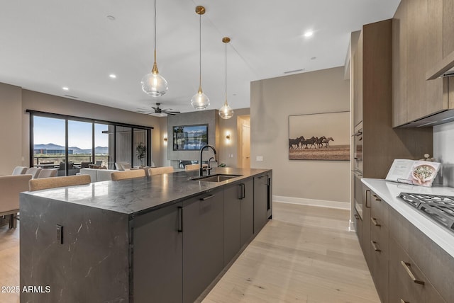 kitchen featuring light wood-type flooring, a kitchen island with sink, a sink, open floor plan, and ceiling fan