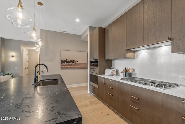 kitchen featuring modern cabinets, a sink, under cabinet range hood, stainless steel appliances, and light wood-style floors