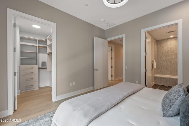 bedroom featuring a spacious closet, visible vents, light wood finished floors, baseboards, and ensuite bath