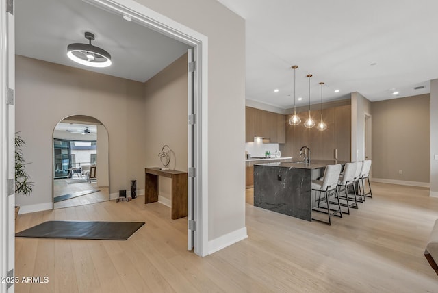 interior space with a kitchen bar, an island with sink, light wood-type flooring, brown cabinets, and modern cabinets