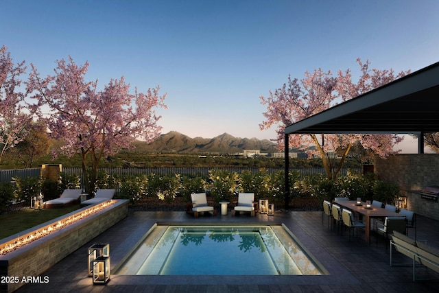 pool at dusk with a patio area, a mountain view, outdoor dining area, and a fenced backyard