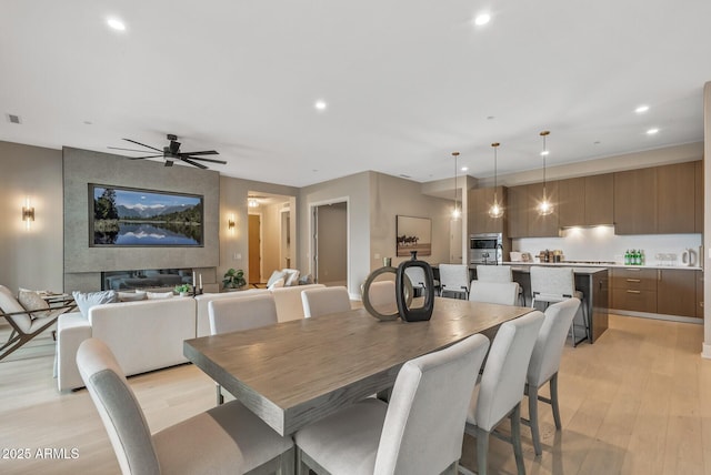 dining room featuring a fireplace, light wood-style flooring, recessed lighting, and ceiling fan