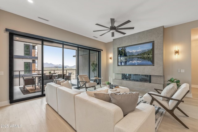 living area with visible vents, light wood-style flooring, baseboards, and a ceiling fan