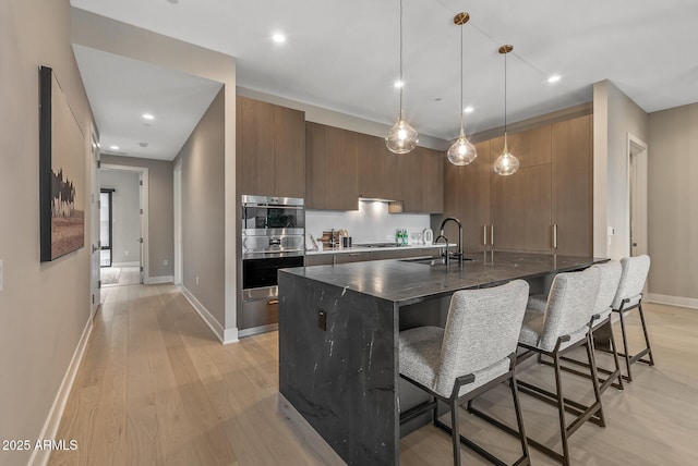 kitchen with a kitchen bar, modern cabinets, light wood-type flooring, and appliances with stainless steel finishes