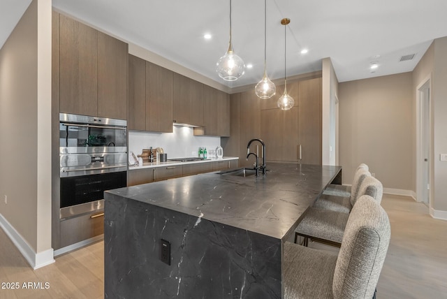 kitchen with visible vents, light wood-type flooring, modern cabinets, a sink, and appliances with stainless steel finishes