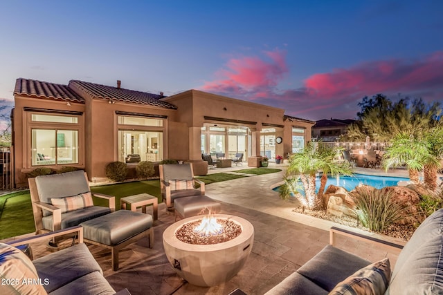 rear view of property featuring an outdoor living space with a fire pit, a patio, stucco siding, a fenced in pool, and a tiled roof