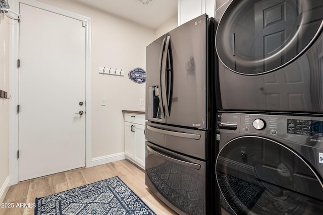 washroom with baseboards, light wood finished floors, stacked washer and dryer, and cabinet space