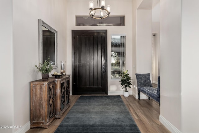 entrance foyer with baseboards, wood finished floors, and a chandelier