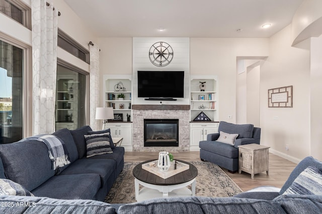 living area with baseboards, a glass covered fireplace, built in features, and light wood-style flooring