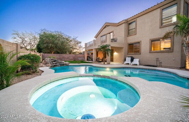 pool at dusk with an in ground hot tub and a patio area