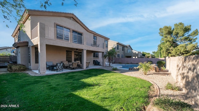 back of house with a lawn, ceiling fan, a balcony, a fenced in pool, and a patio area