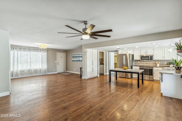 unfurnished living room with baseboards, wood finished floors, and a ceiling fan