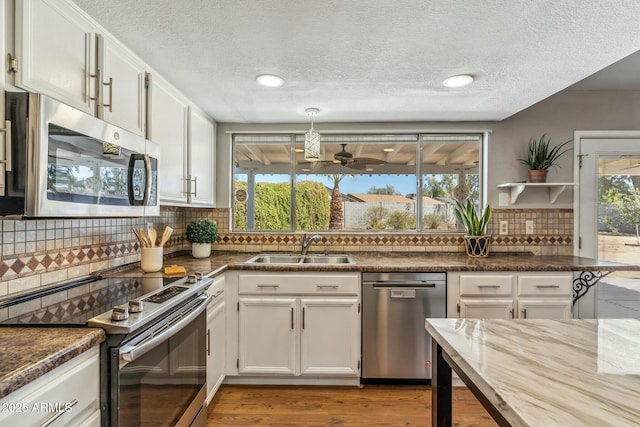 kitchen with a sink, stainless steel appliances, light wood-style floors, white cabinets, and decorative backsplash