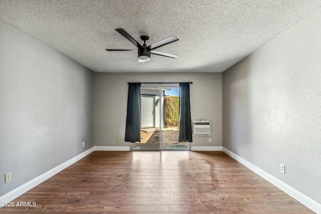 spare room with a ceiling fan, wood finished floors, baseboards, an AC wall unit, and a textured ceiling