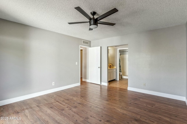 unfurnished bedroom with visible vents, ensuite bathroom, a textured ceiling, wood finished floors, and baseboards