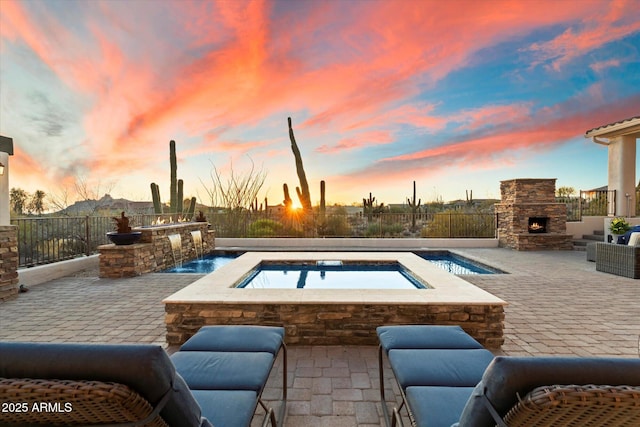 pool at dusk featuring a fenced in pool, an in ground hot tub, a fenced backyard, an outdoor stone fireplace, and a patio area