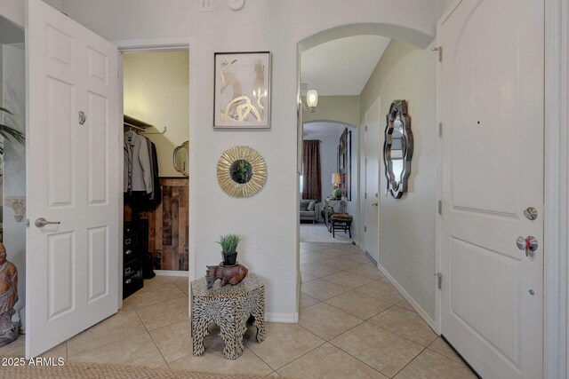 hall featuring arched walkways, light tile patterned flooring, and baseboards