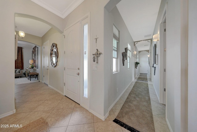 foyer with arched walkways, ornamental molding, light tile patterned flooring, and baseboards