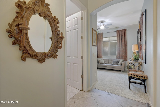 corridor with light tile patterned floors, baseboards, arched walkways, and light colored carpet