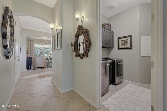 interior space with light tile patterned floors, baseboards, arched walkways, washing machine and clothes dryer, and crown molding