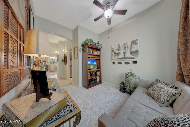 carpeted living room featuring ceiling fan, arched walkways, vaulted ceiling, and baseboards