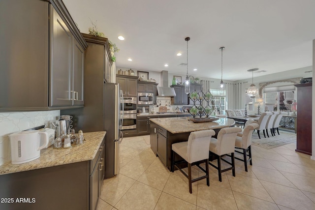 kitchen with a center island, a breakfast bar area, tasteful backsplash, appliances with stainless steel finishes, and wall chimney range hood