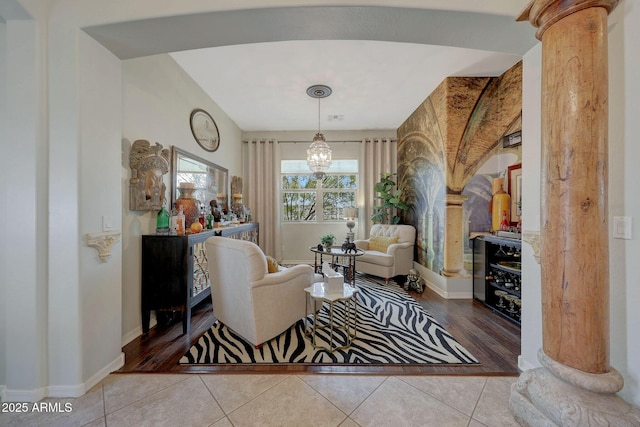 sitting room featuring a chandelier, baseboards, tile patterned flooring, and ornate columns