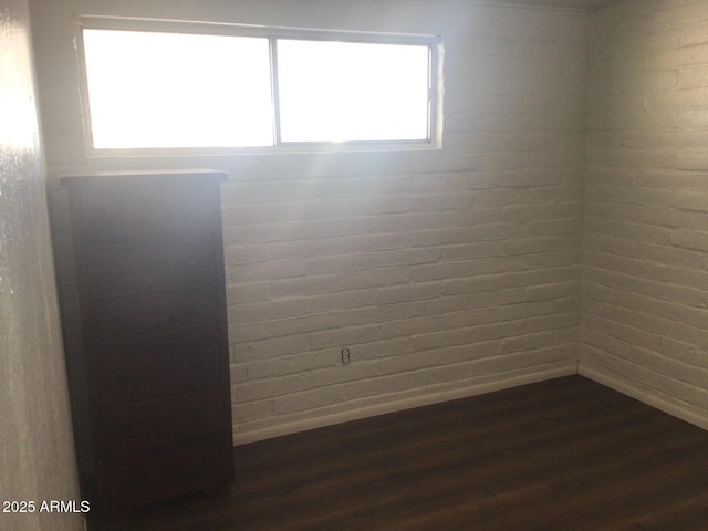 spare room featuring dark hardwood / wood-style floors and brick wall