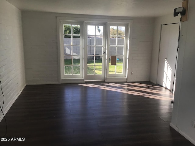 spare room with brick wall, plenty of natural light, and dark hardwood / wood-style floors