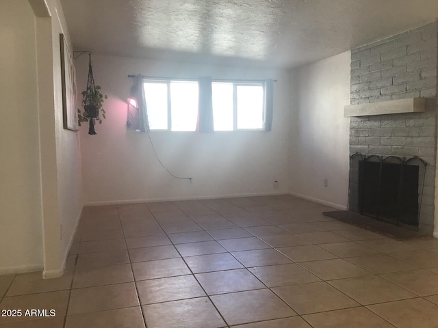 unfurnished living room with a brick fireplace, light tile patterned floors, and a textured ceiling