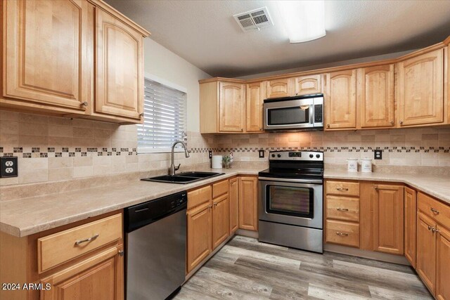 kitchen with sink, backsplash, stainless steel appliances, and light hardwood / wood-style floors