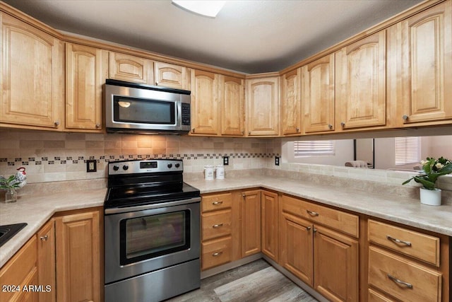 kitchen featuring stainless steel appliances, light wood-type flooring, and backsplash