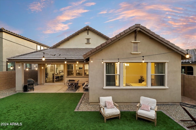 back house at dusk featuring a lawn and a patio area