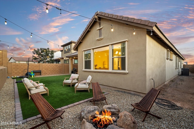 back house at dusk featuring an outdoor living space with a fire pit and a lawn