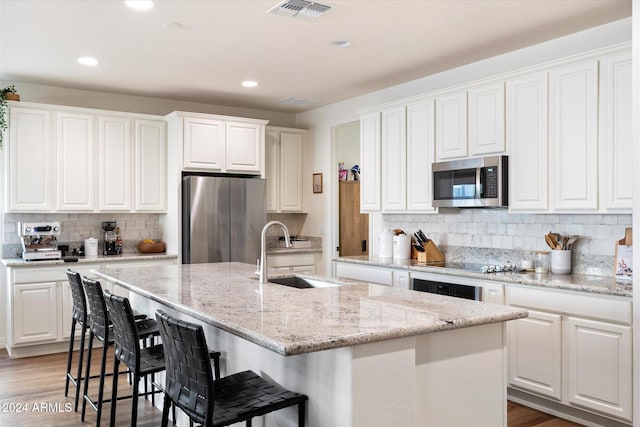 kitchen with white cabinets, a kitchen island with sink, sink, and appliances with stainless steel finishes