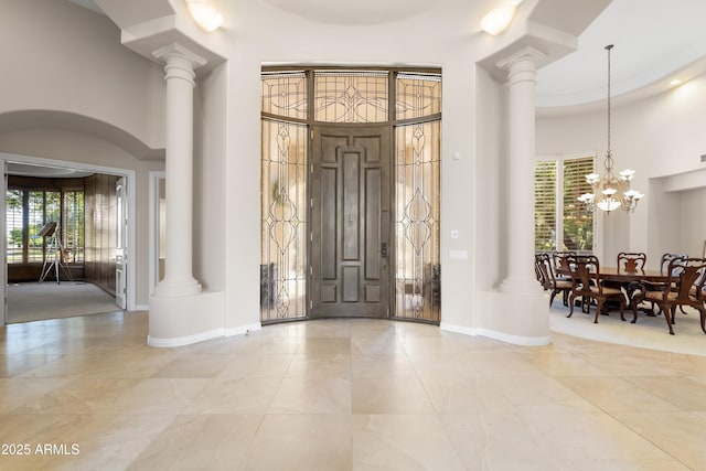 entryway featuring a high ceiling, ornate columns, marble tiled floors, and a chandelier