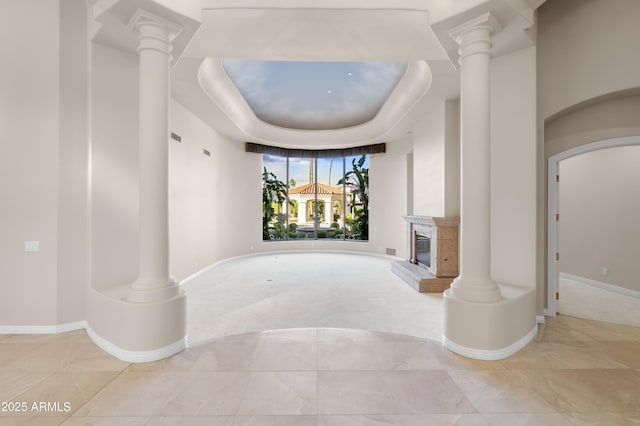 unfurnished living room with decorative columns, baseboards, carpet floors, and a glass covered fireplace