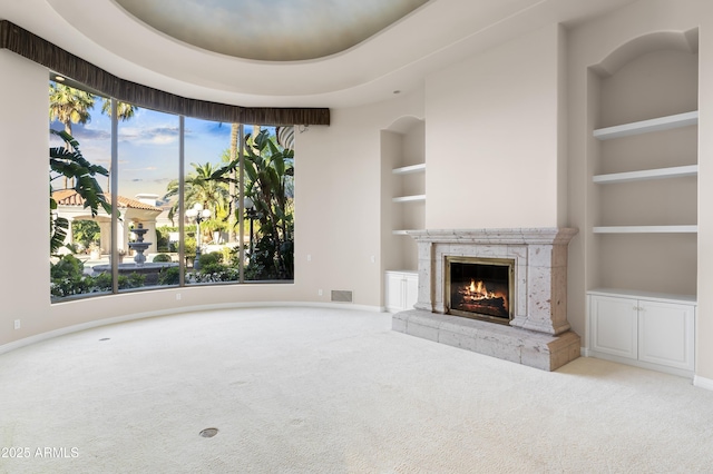 unfurnished living room featuring carpet flooring, built in shelves, a high end fireplace, and baseboards