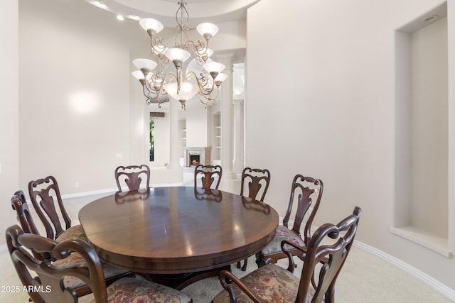 carpeted dining space with a chandelier, built in shelves, a warm lit fireplace, and baseboards
